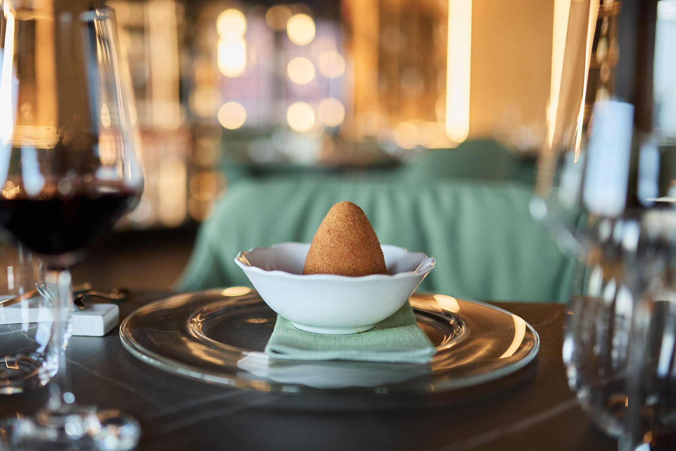 Zlatni arancini u beloj činiji na elegantnom restoranskom stolu.