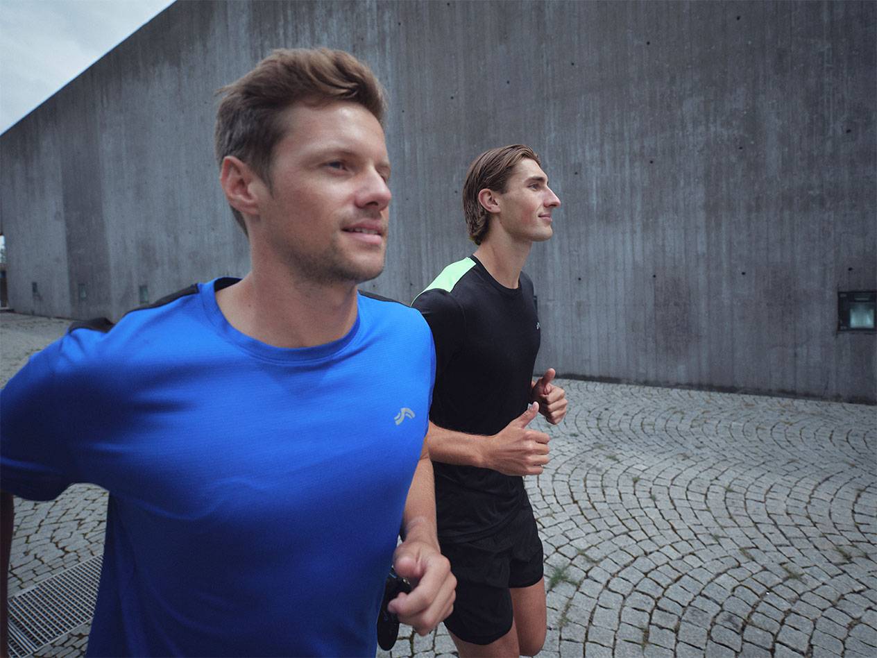 Два мушкарца трче у спортским мајицама и шортсевима, један плави и један црни.