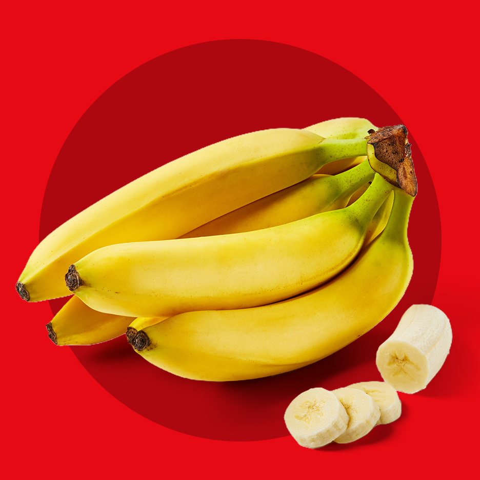Sveže žute banane u grozdu sa isečenim kolutovima na crvenoj pozadini.