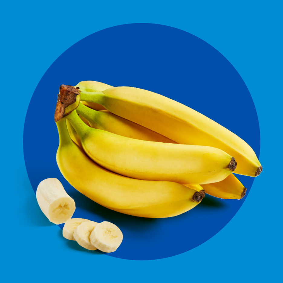 Sveže žute banane, cele i isečene na kolutove, na plavoj pozadini.
