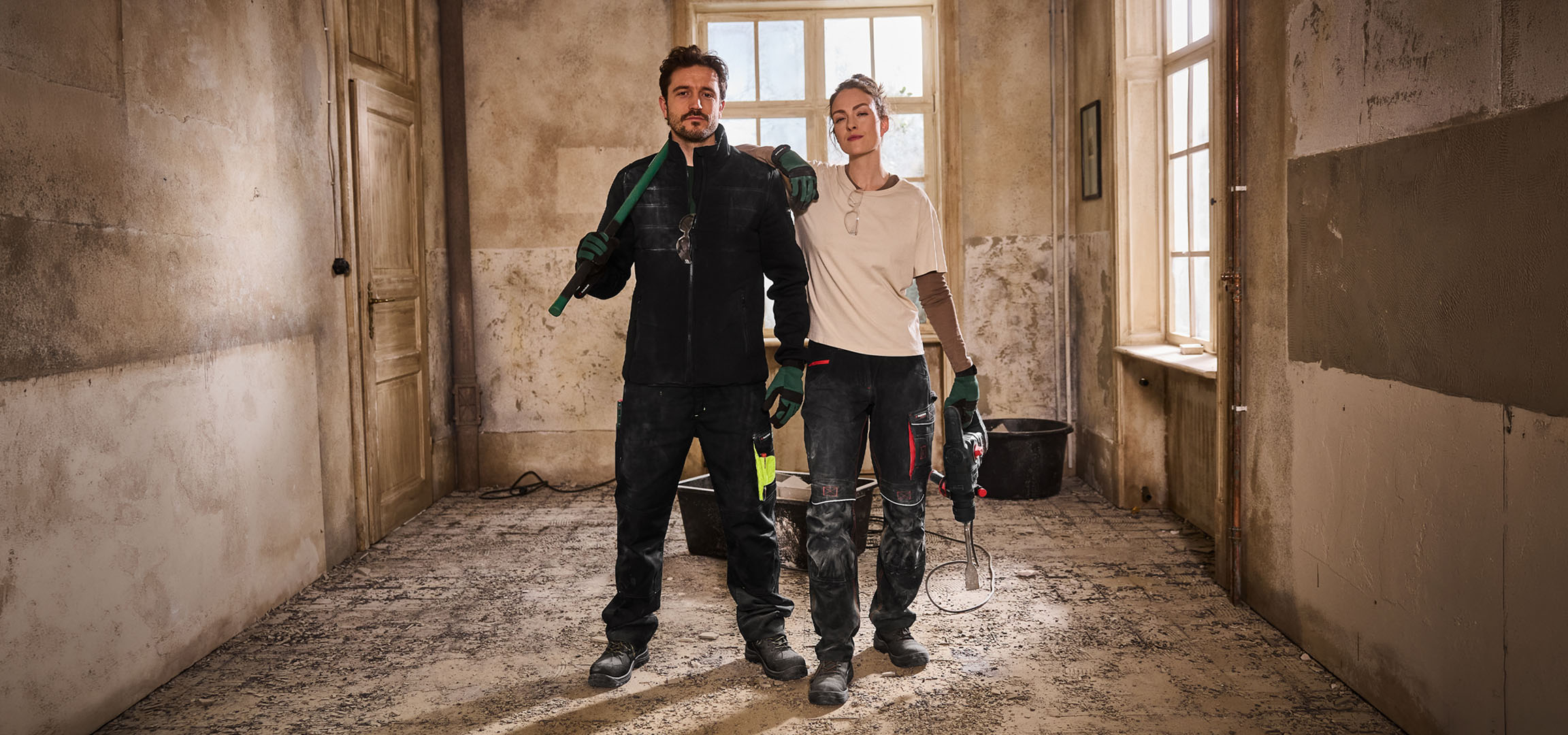 Dva građevinska radnika u radnoj odeći sa alatom na gradilištu.