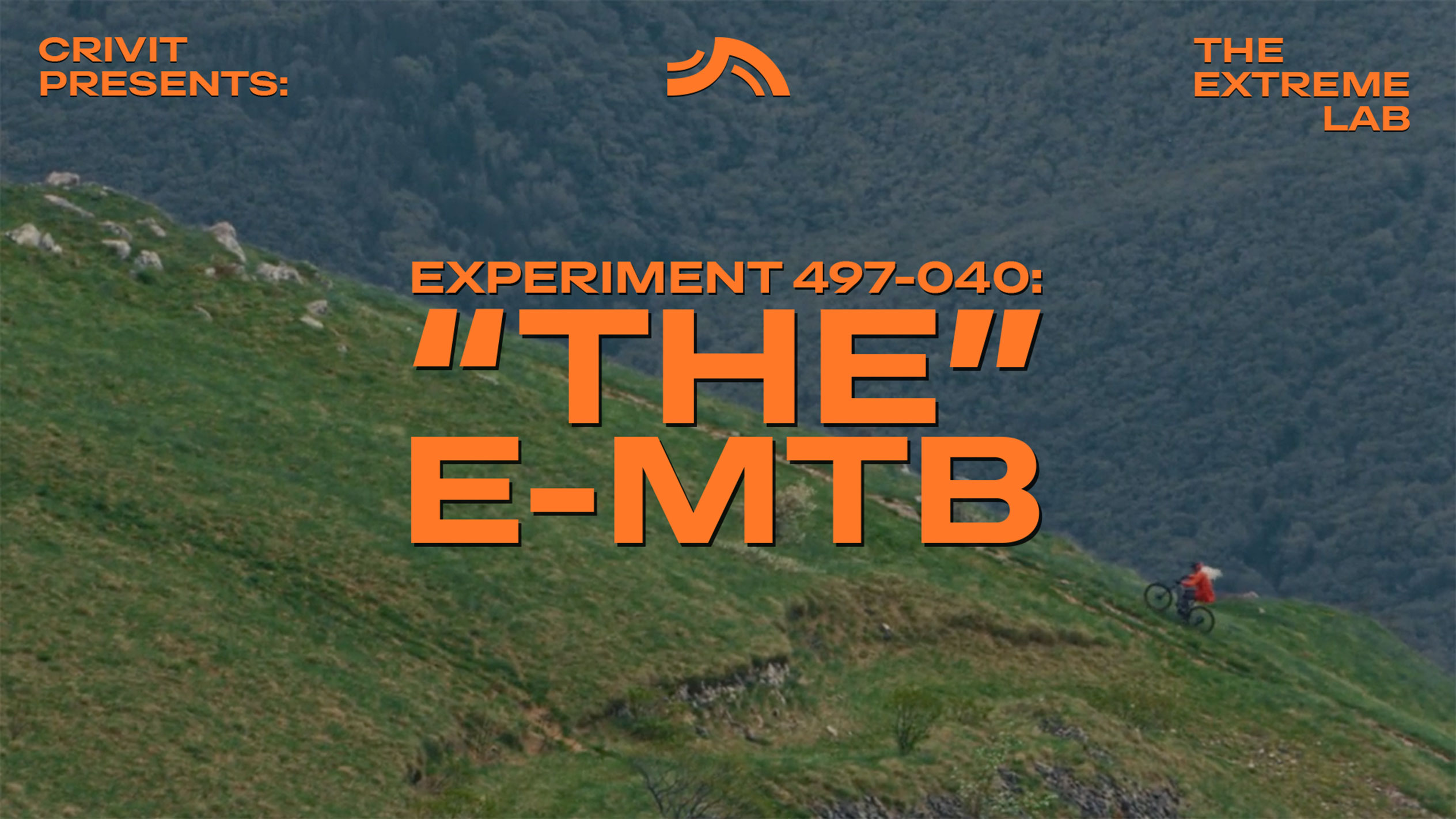 Biciklista na planinskom biciklu na travnatoj padini, sa tekstom 'THE E-MTB' i 'THE EXTREME LAB'.