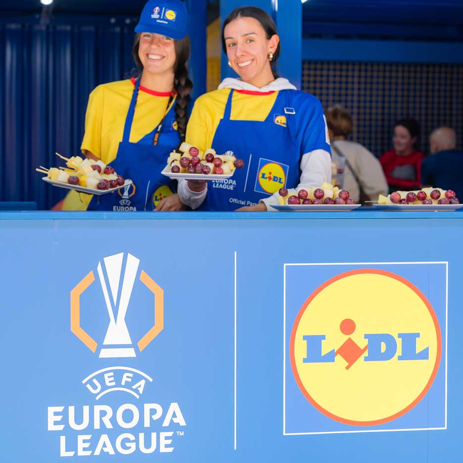 Dve nasmejane žene u Lidl keceljama nude voće na štapićima na događaju UEFA Lige Evrope.