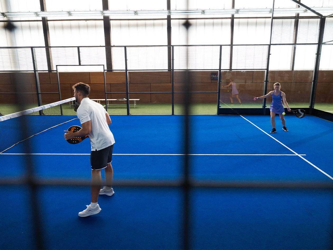 Muškarac i žena igraju padel na plavom terenu sa reketima i lopticom.
