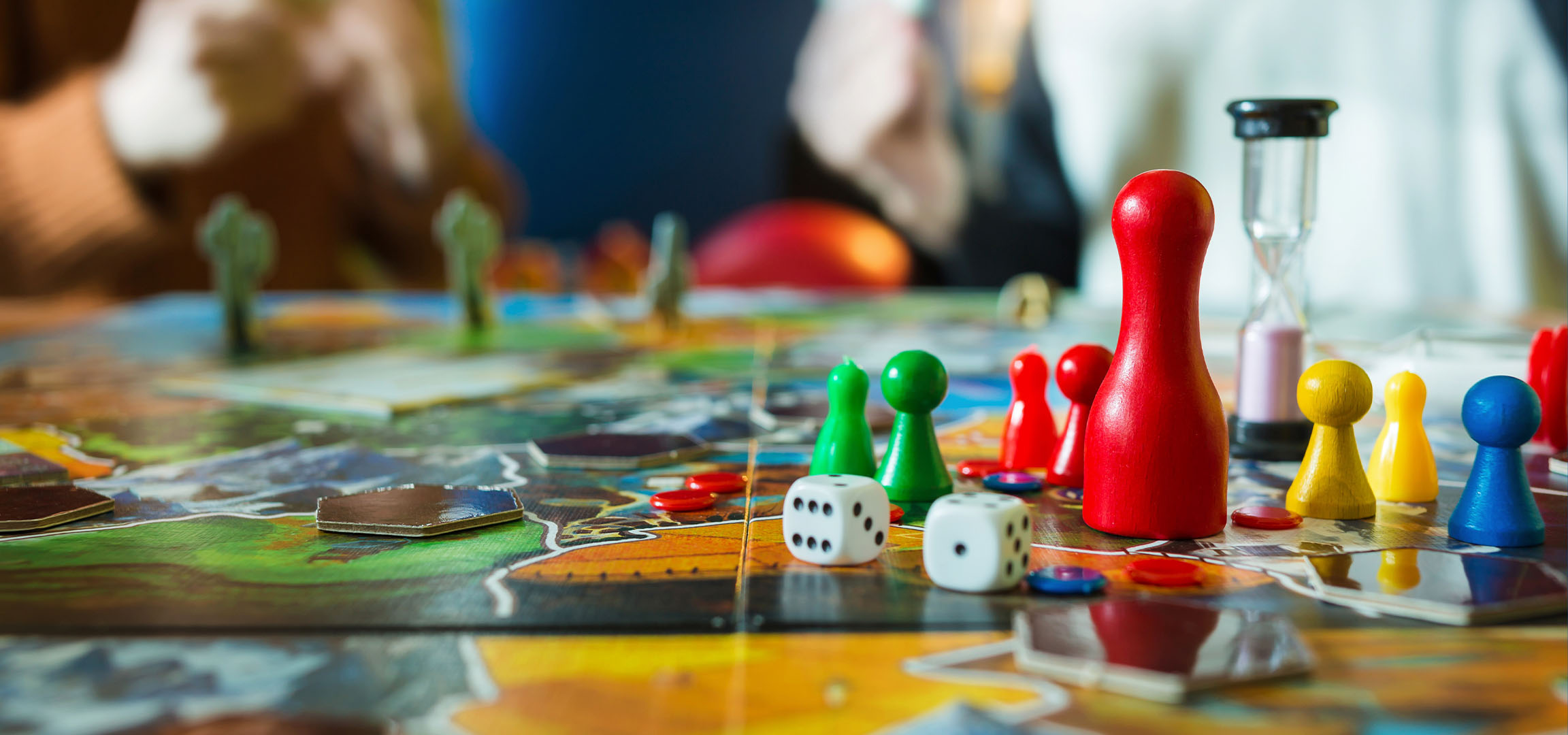 Šarene figure za društvene igre, uključujući crvene, zelene, žute i plave pijune, sa kockicama.