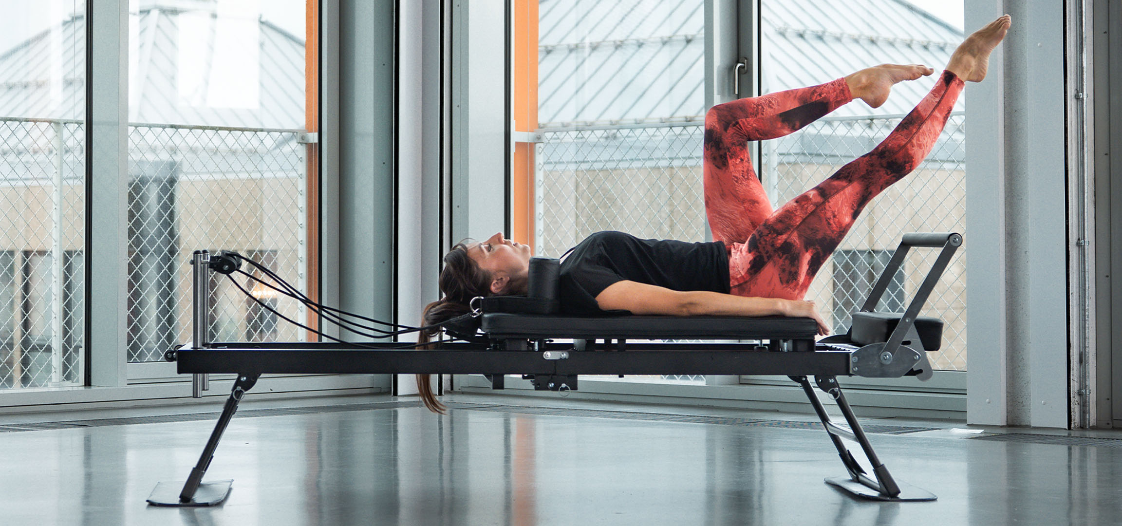 Žena vežba Pilates na reformer spravi, sa fitnes dodacima u blizini.