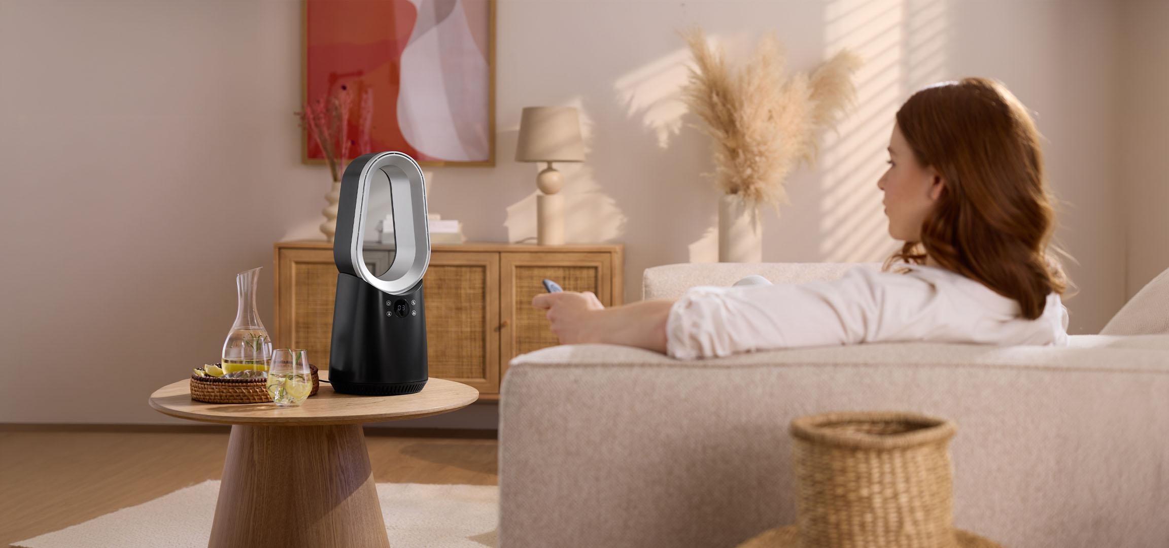 Žena na sofi sa daljinskim upravljačem, moderni ventilator i pića na stolu.