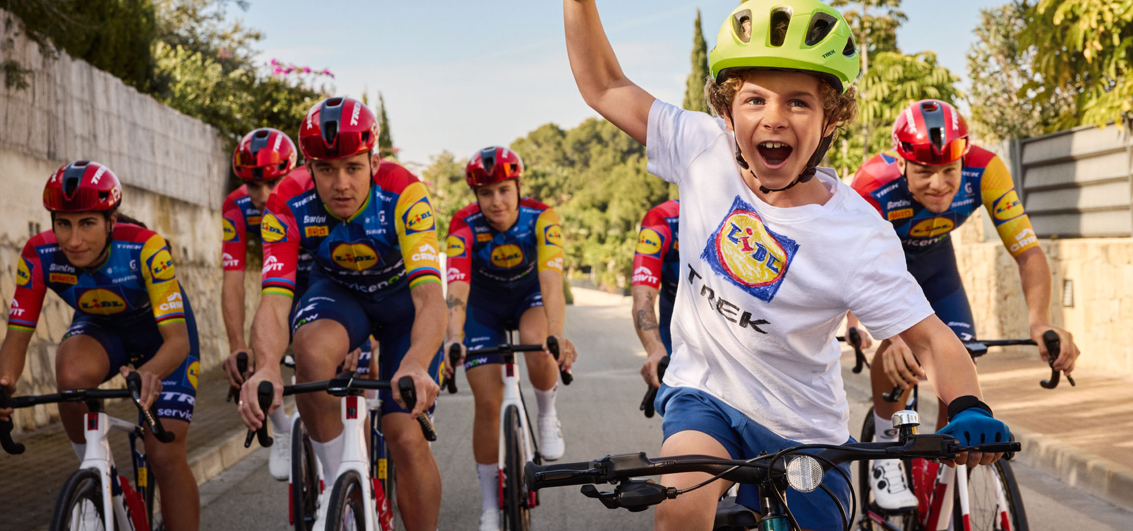 Dete sa kacigom i majicom sa Lidl logom, okruženo biciklistima.