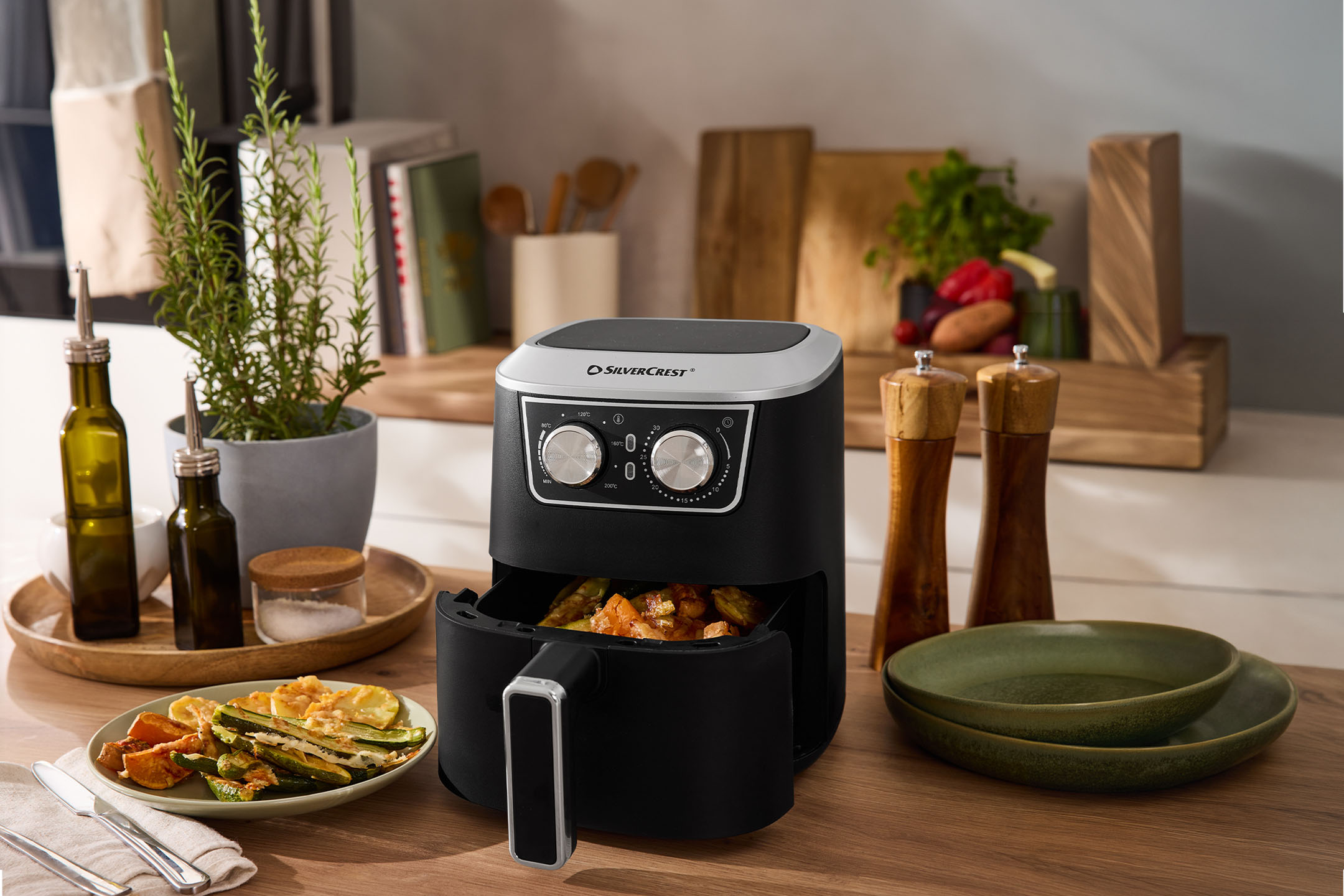 Crni friteza na vruć vazduh sa povrćem, začinima i posuđem na drvenoj radnoj ploči.