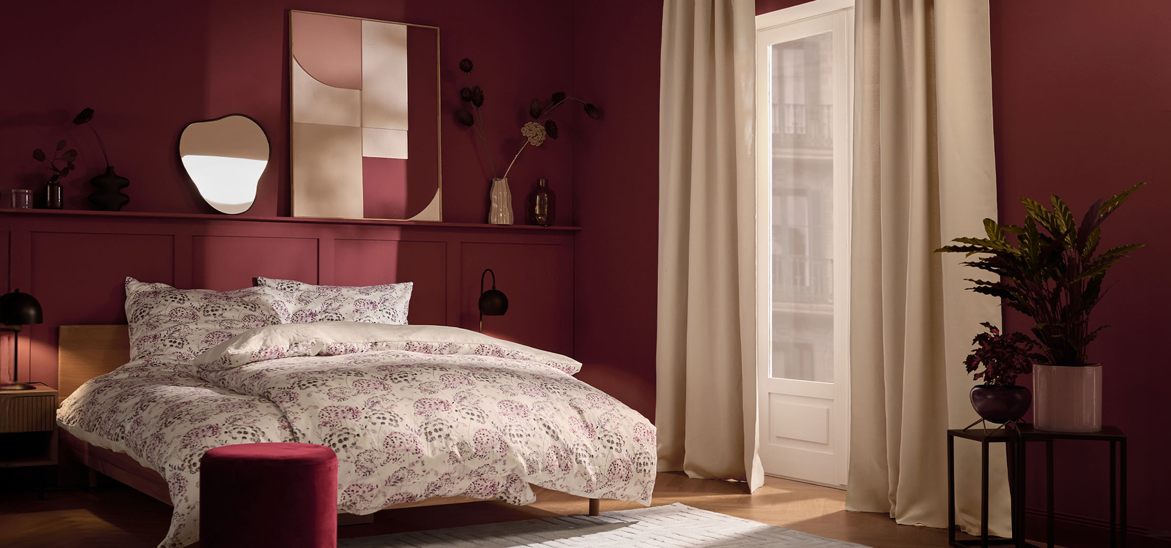 Spavaća soba sa tamnocrvenim zidovima, krevetom sa belom posteljinom sa cvetnim dezenom i biljkama.