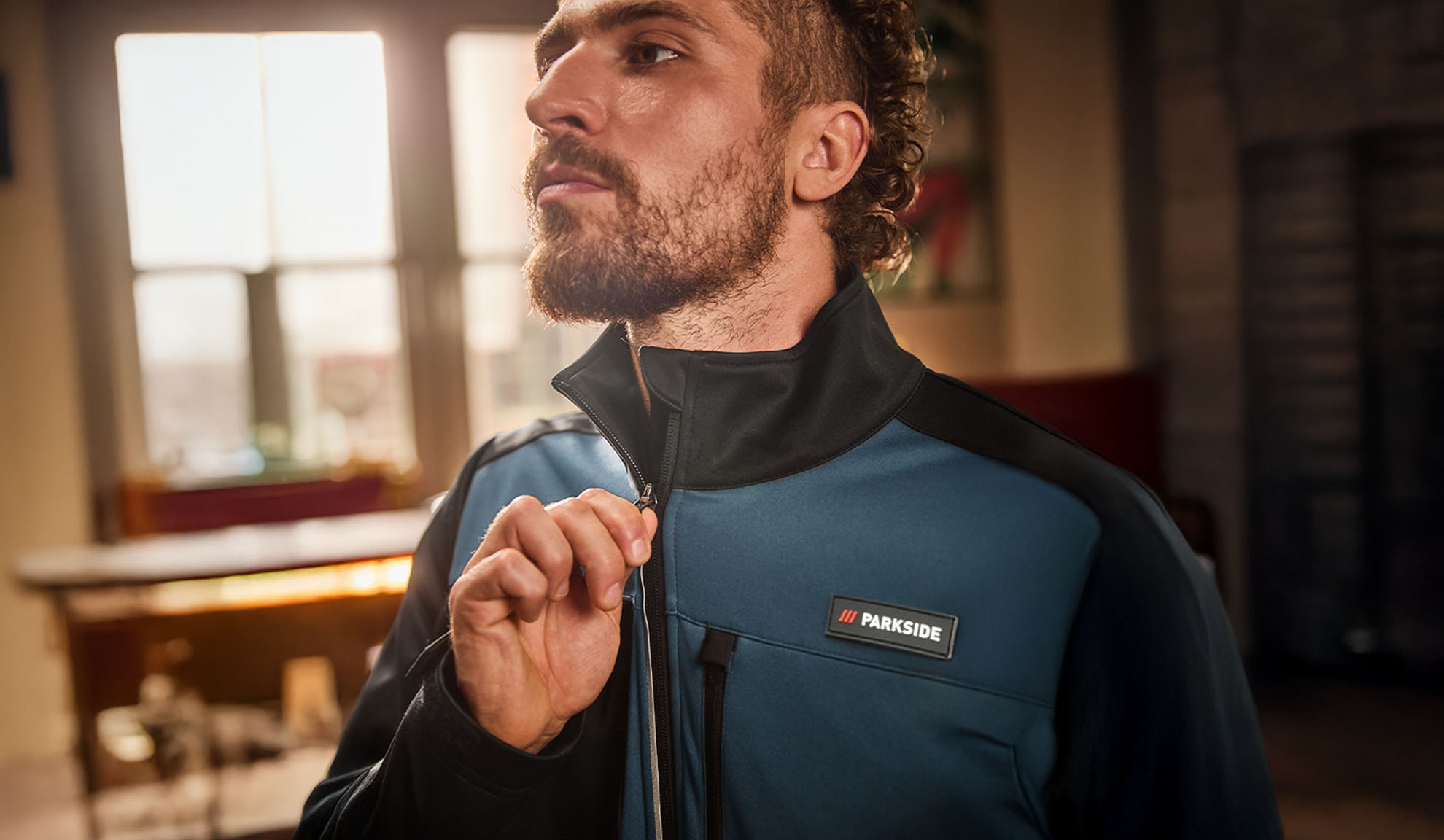 Muškarac u plavo-crnoj Parkside radnoj jakni, zakopčava je.