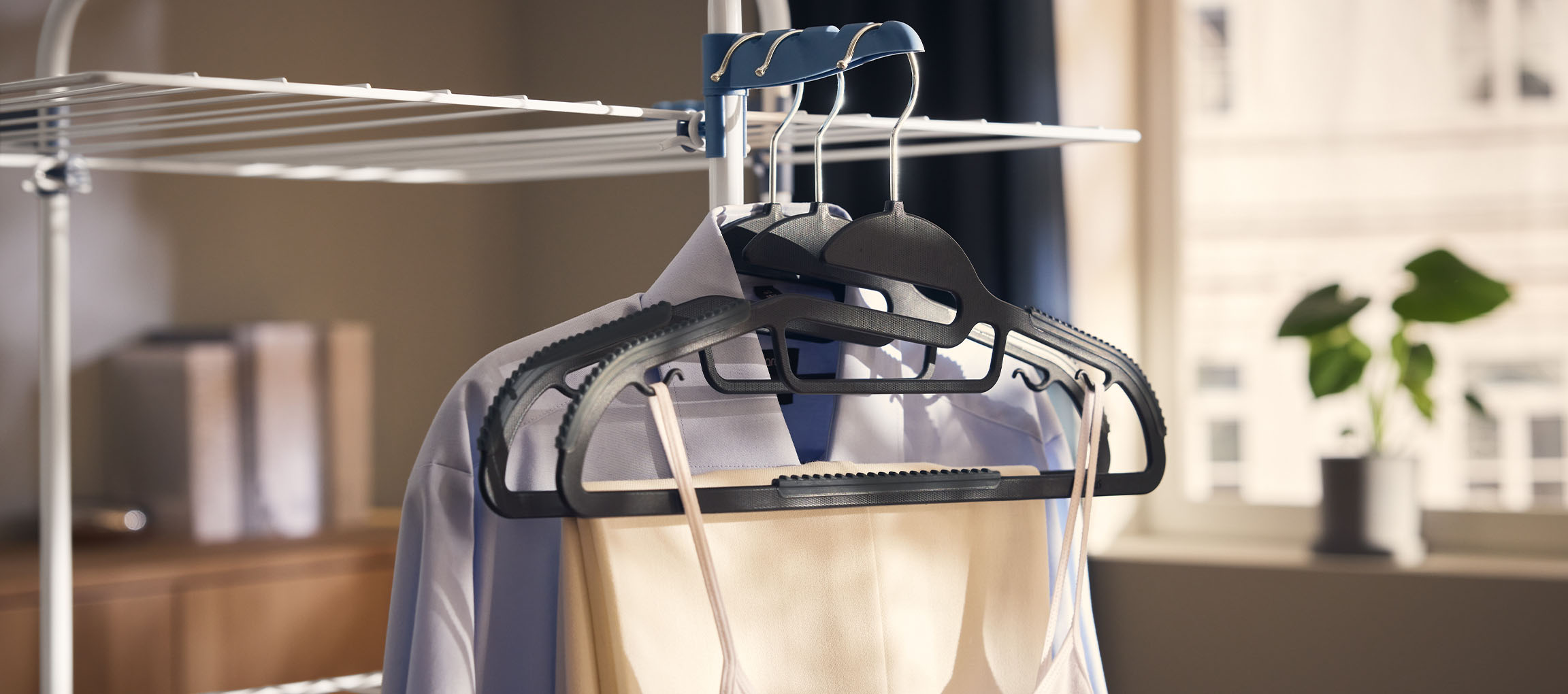 Odeća na vešalicama na sušilici, sa biljkom u pozadini.