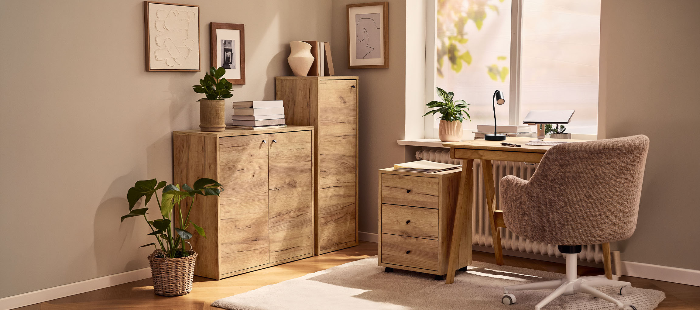 Kućna kancelarija sa drvenim ormarićima, stolom i stolicom, ukrašena biljkama i slikama.