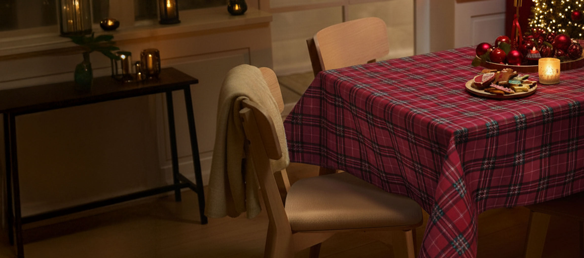 Božićna postavka stola sa crvenim kariranim stolnjakom, stolicama i božićnim kolačićima.