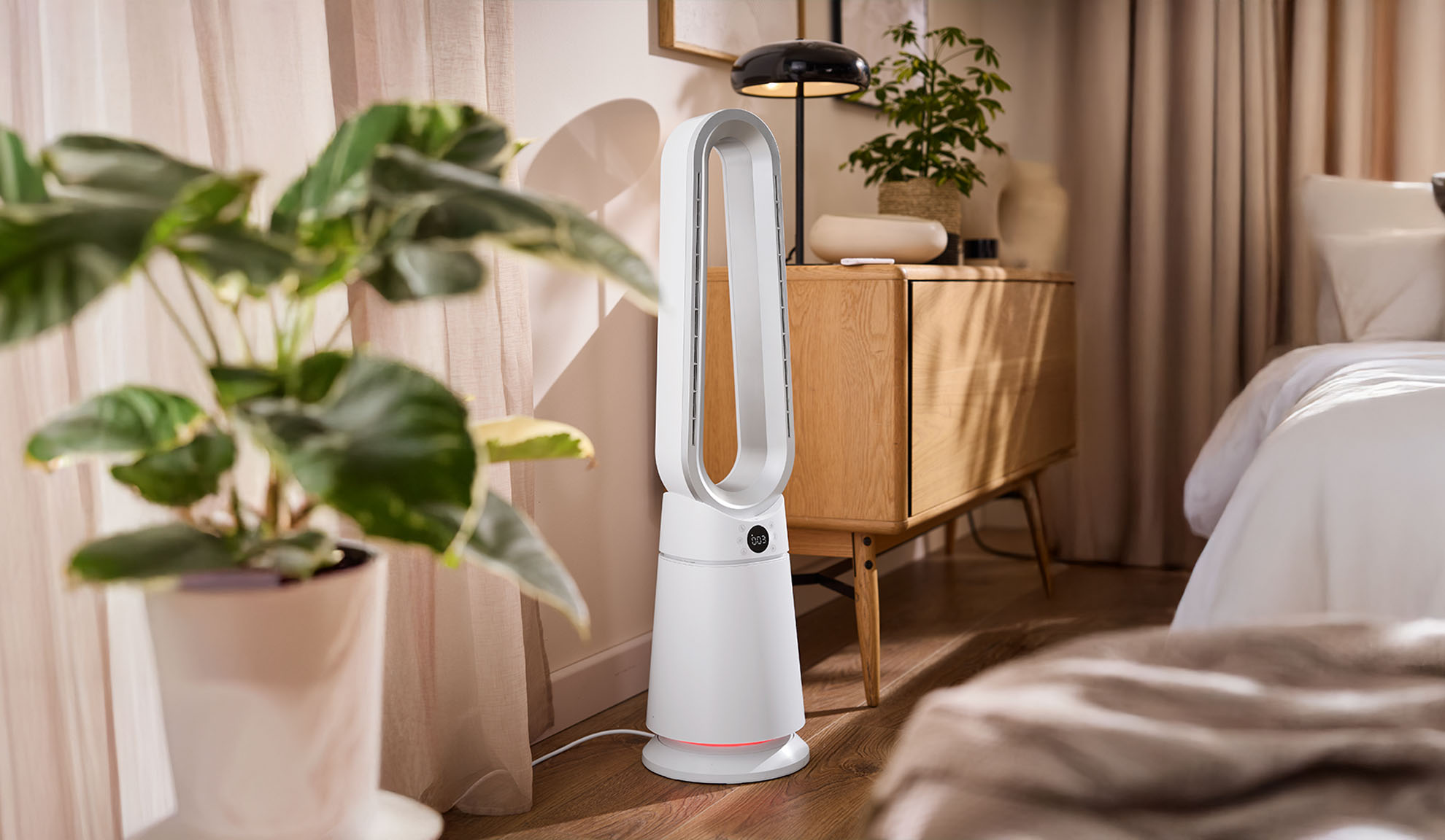 Beli toranj ventilator u modernoj spavaćoj sobi sa biljkama i drvenim nameštajem.