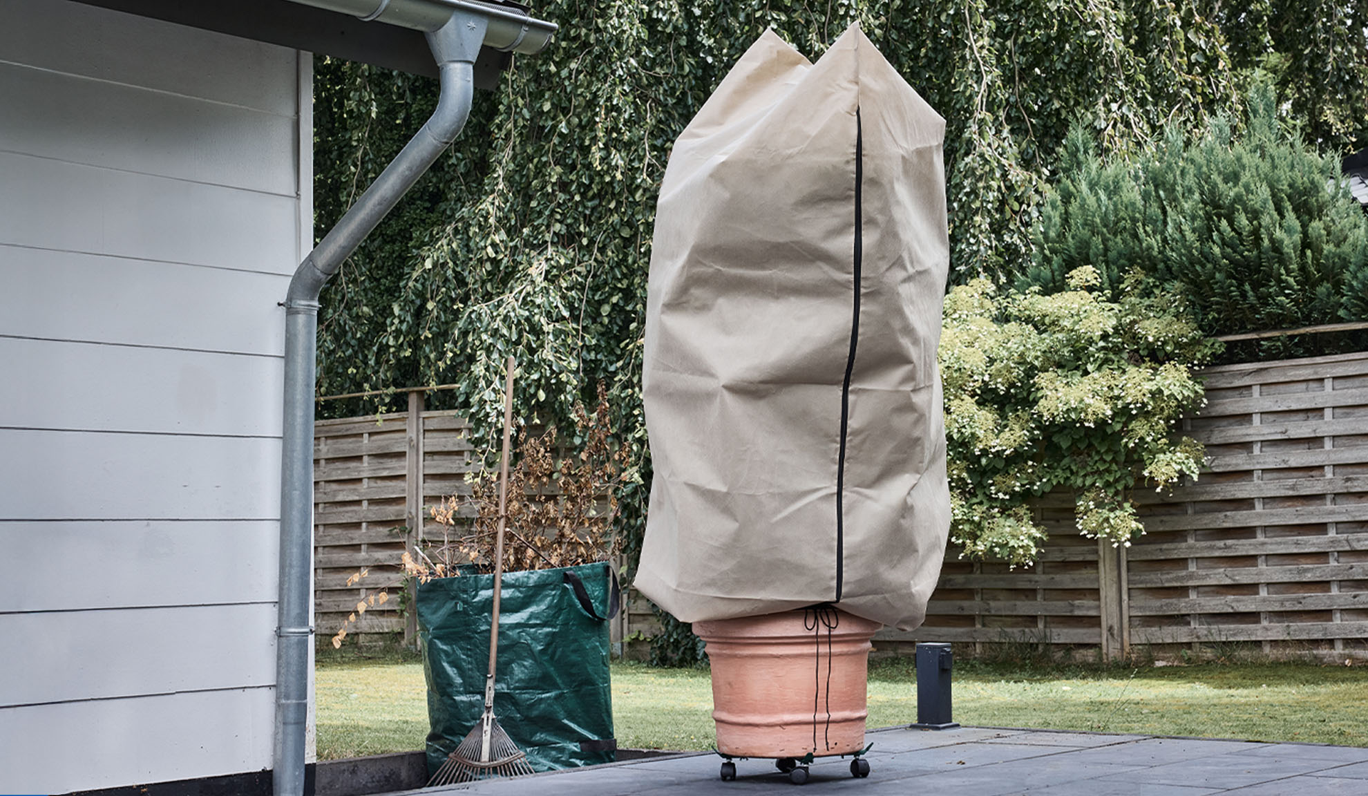 Prekrivač za biljke u saksiji na terasi sa olukom i grabuljama.