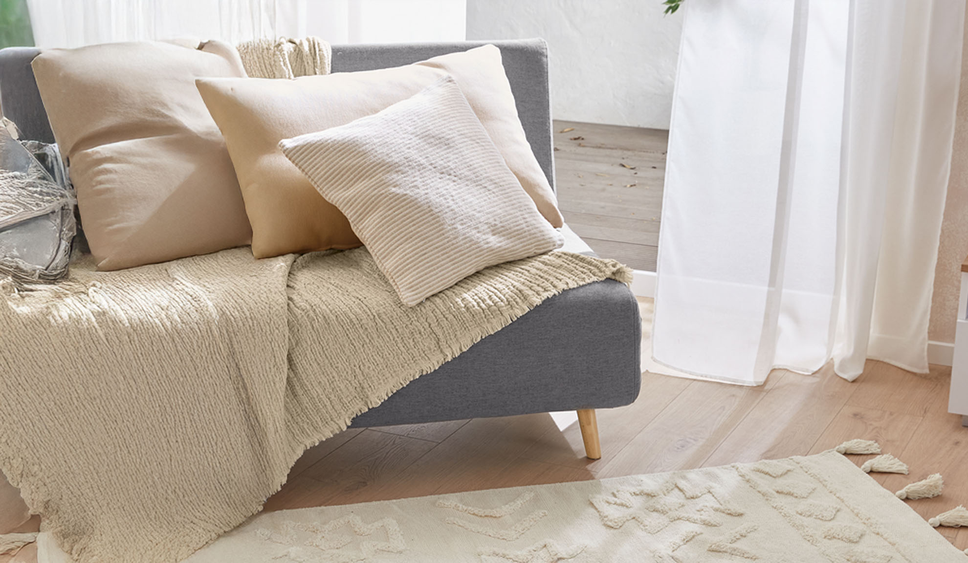 Siva sofa sa bež jastucima i teksturiranim prekrivačem u svetloj dnevnoj sobi.