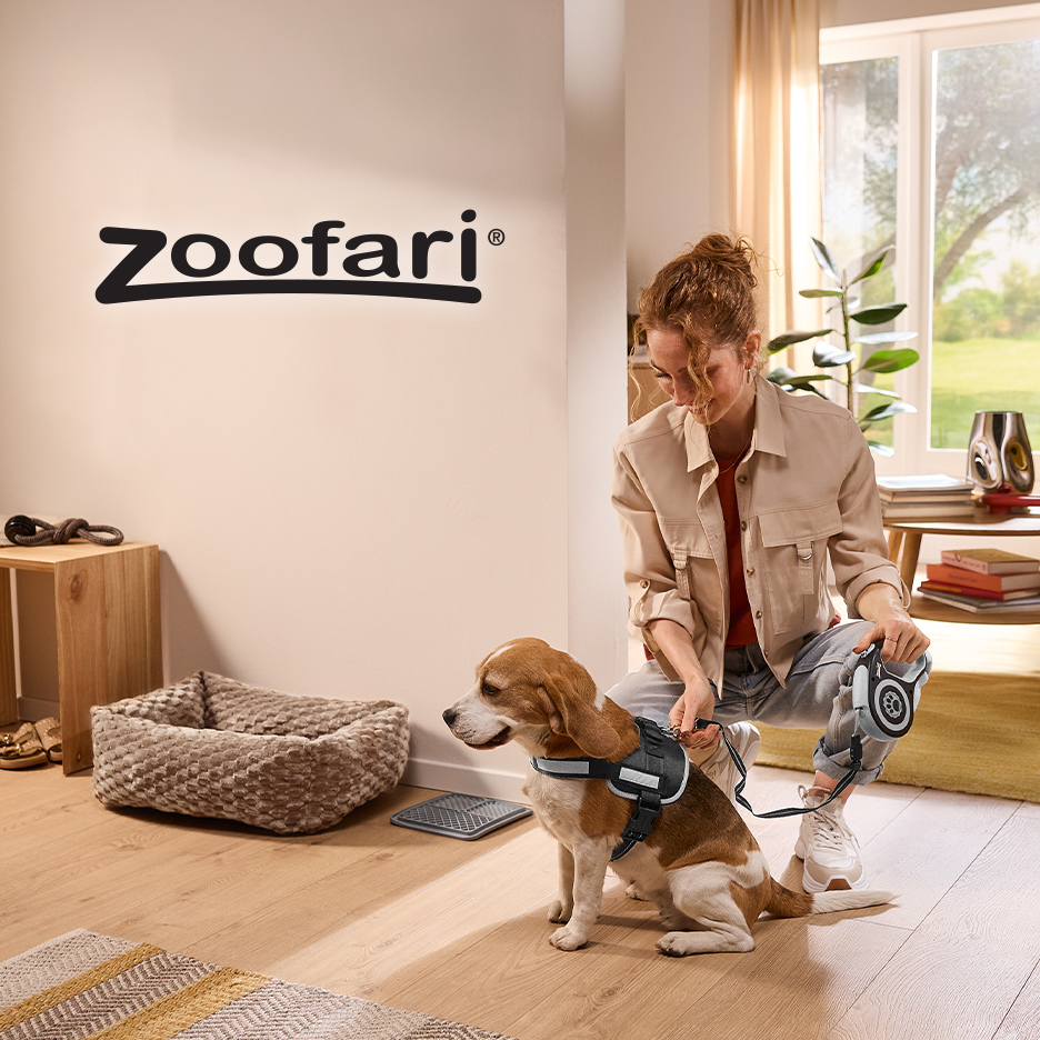 Žena stavlja povodac psu sa oprsnicom, u pozadini je krevet za pse i natpis „Zoofari“.