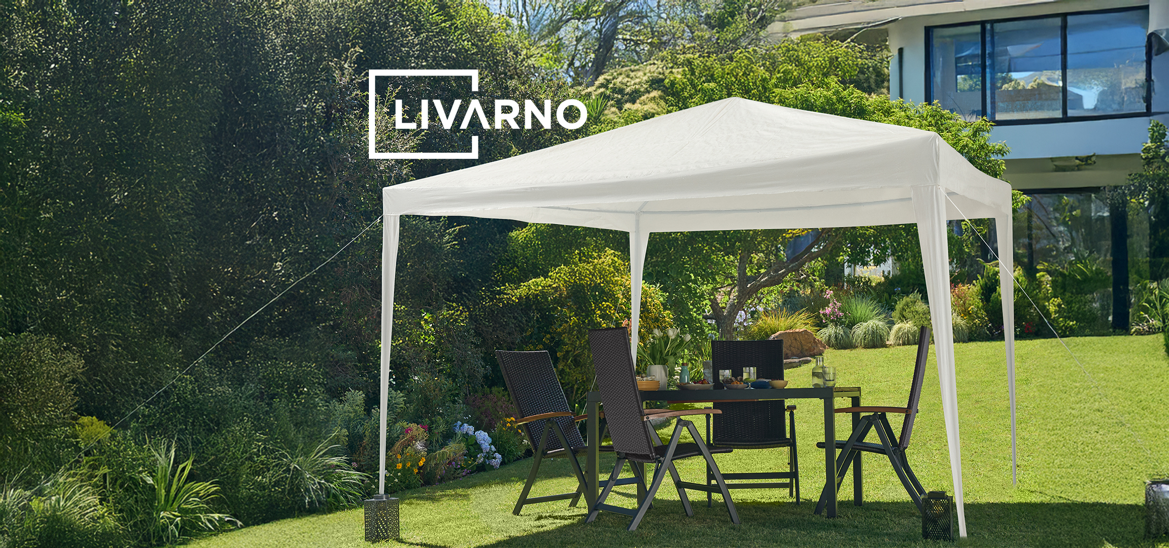 Beli šator za zabave i sivi suncobran sa baštenskim nameštajem u zelenom vrtu.