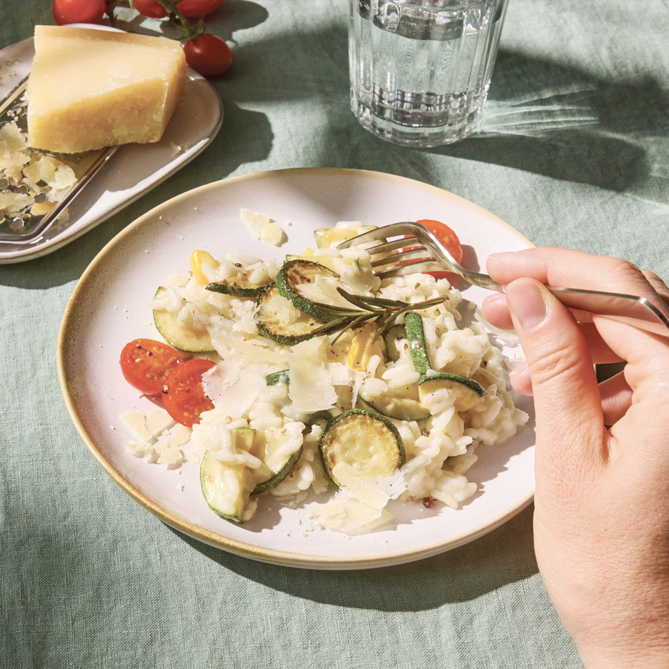 Rižoto sa tikvicama, paradajzom i parmezanom, sa rukom koja ga jede viljuškom.