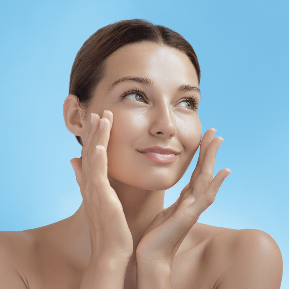 Žena sa negovanom kožom lica, nanosi kremu na obraze.