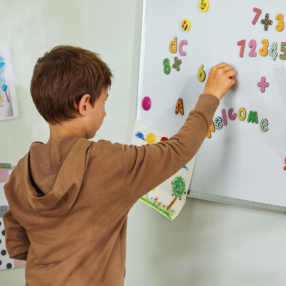 Dečak se igra sa magnetnim slovima i brojevima na beloj tabli.