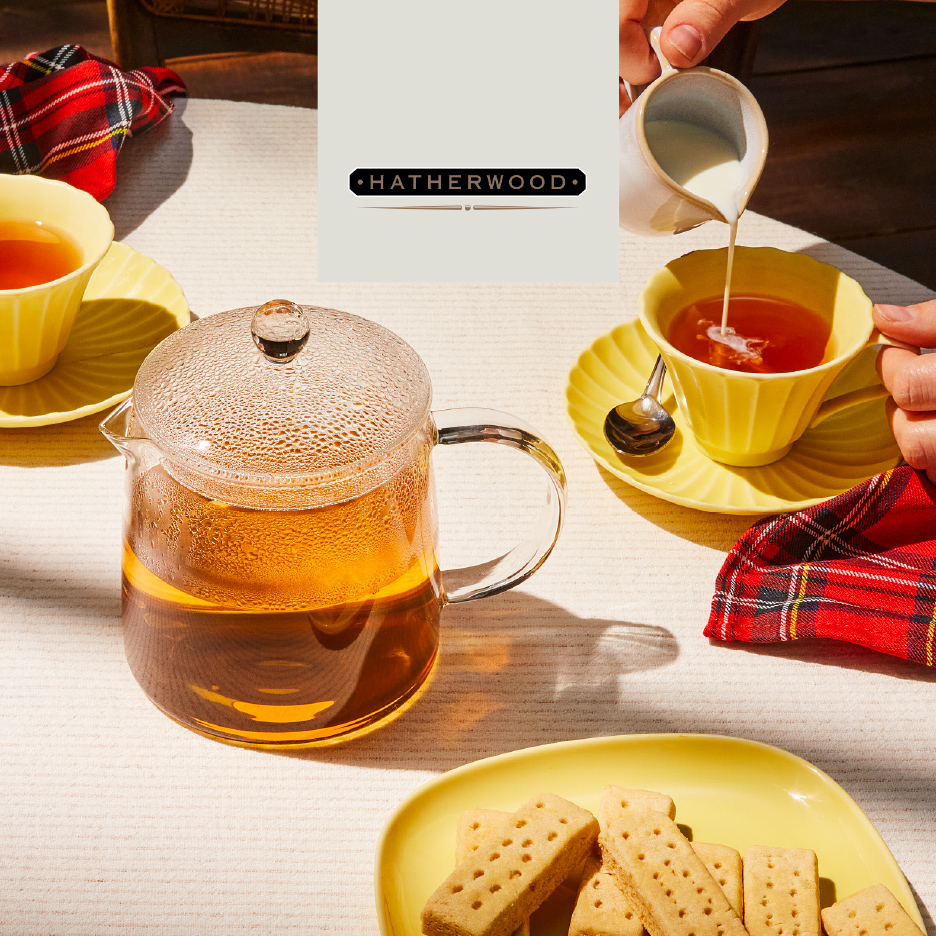 Čajnik i šoljice čaja sa mlekom i keksom na stolu, sa kariranom tkaninom.