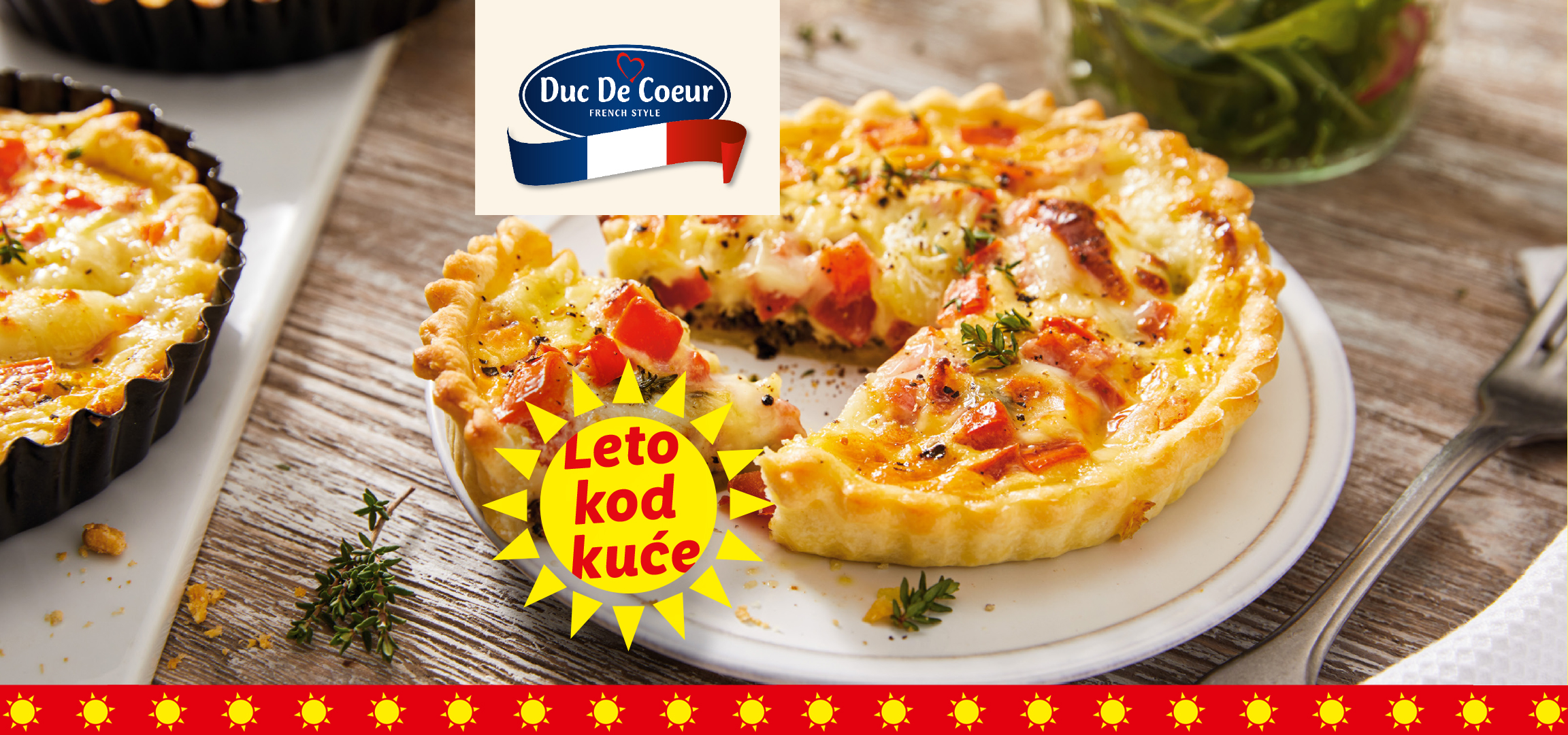 Kiš sa paradajzom i sirom, uz pakovanja flammekueche i krompir kuglica, sa natpisom „Leto kod kuće“.