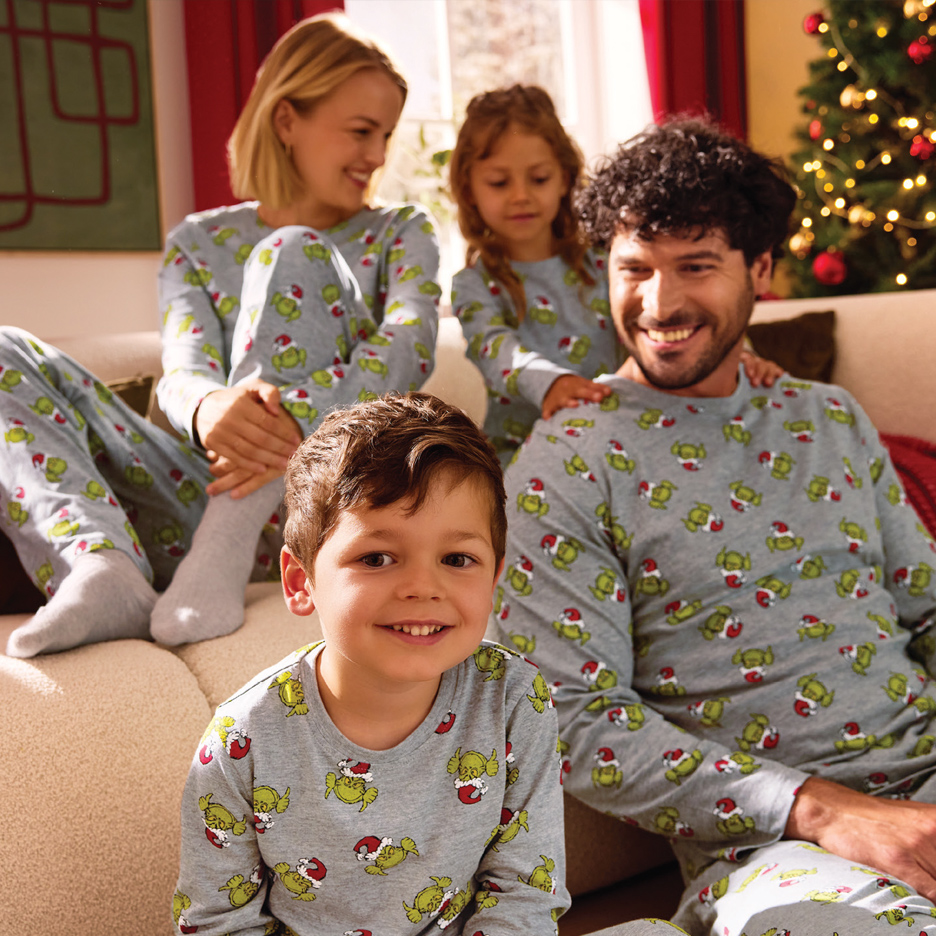 Porodica u sivim božićnim pidžamama sa Grinčom, sedi na kauču pored jelke.