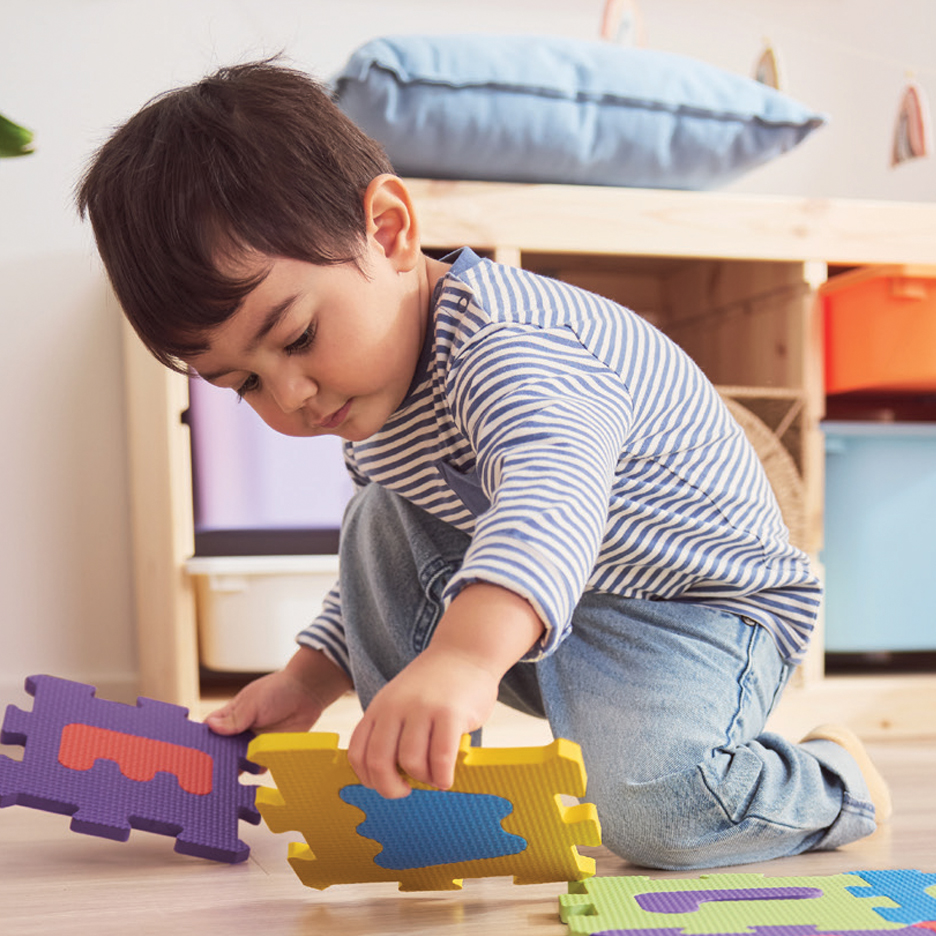 Dečak se igra sa šarenim podnim slagalicama u sobi.