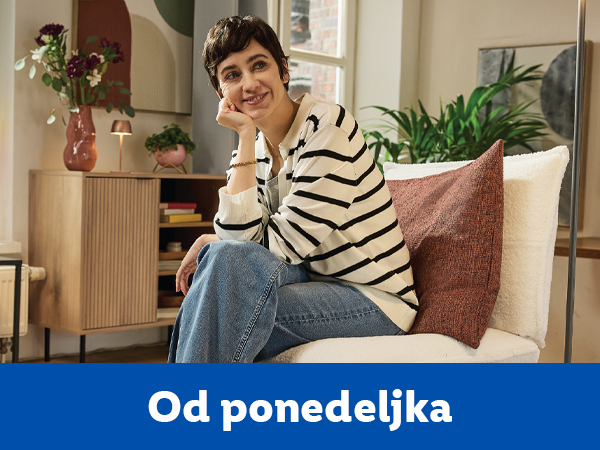 Žena sedi na stolici u dnevnoj sobi, okružena nameštajem i dekoracijom.