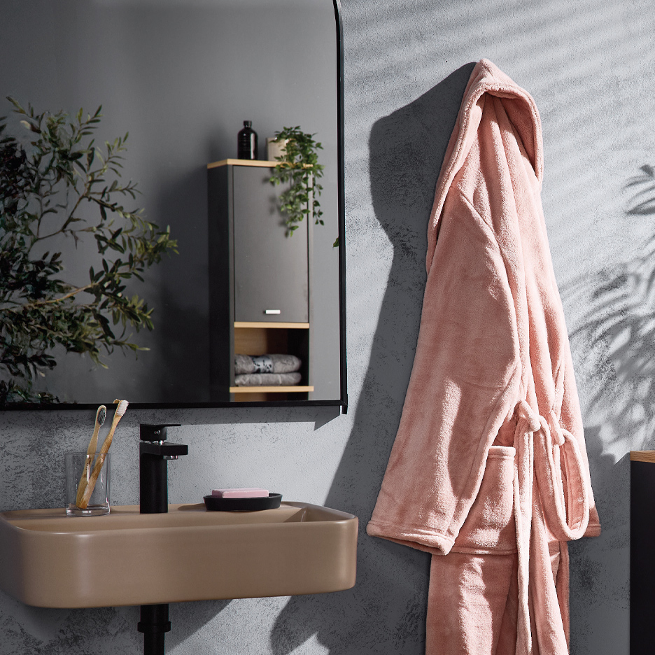 Kupatilo sa bež lavaboom, crnom slavinom, ogledalom i ružičastim bade-mantilom.