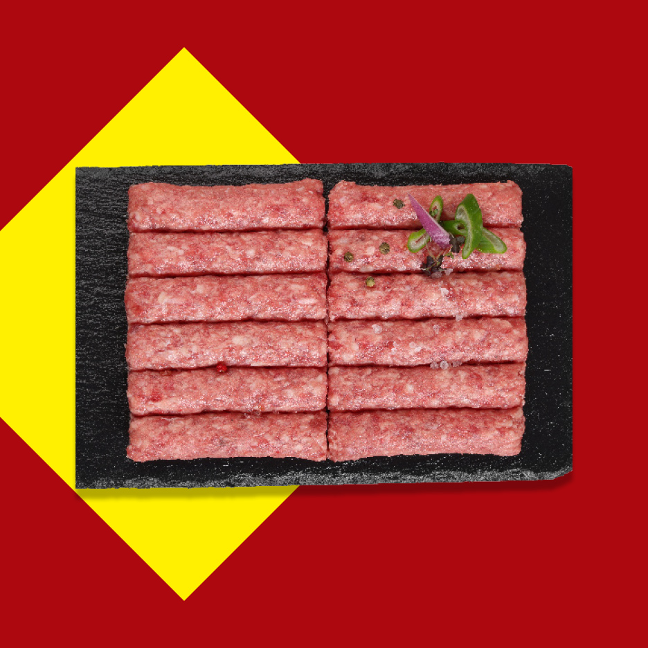 Sveži ćevapi na crnoj ploči, ukrašeni začinima, na crveno-žutoj pozadini.