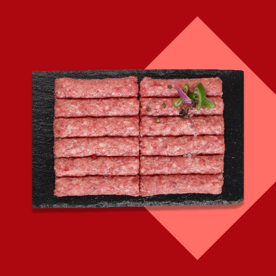 Sveži ćevapi na crnoj ploči, ukrašeni začinima.