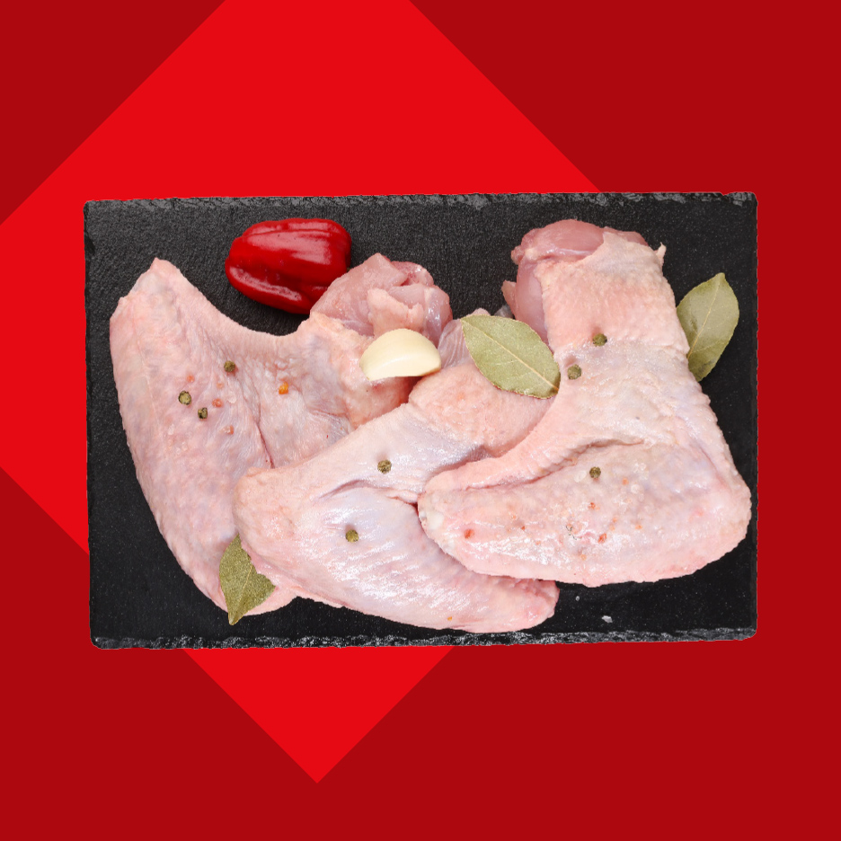 Sveža pileća krilca sa začinima, belim lukom i paprikom na crnoj ploči.