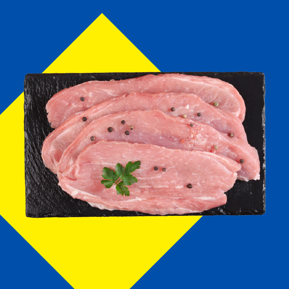 Sveži svinjski odresci sa biberom i peršunom na crnoj ploči, na plavo-žutoj pozadini