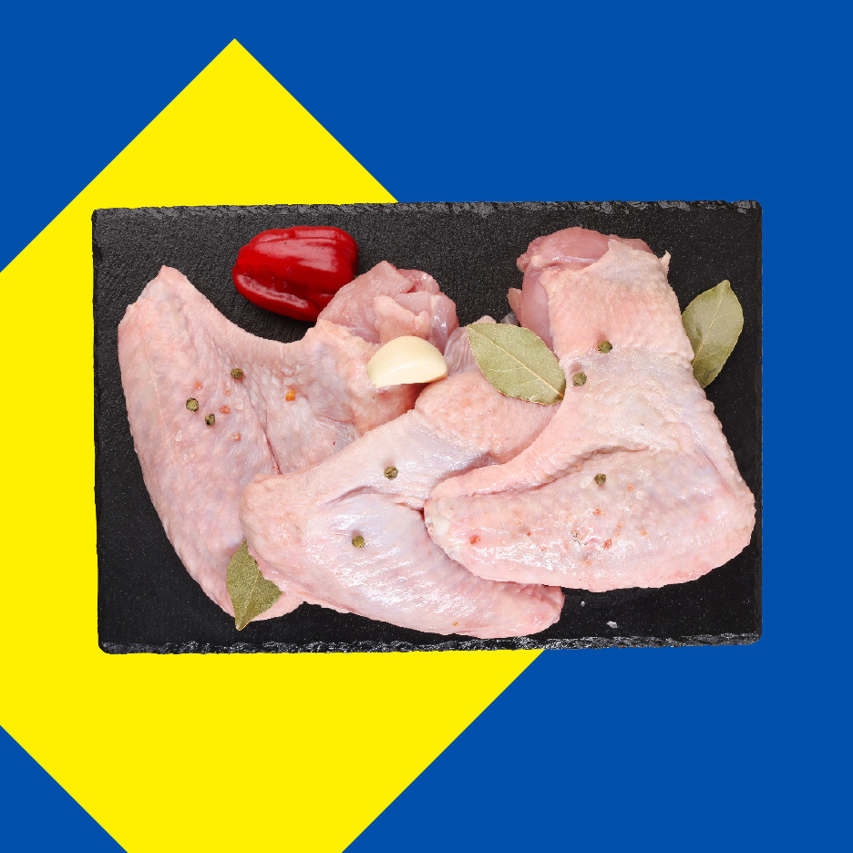 Sveža pileća krilca sa začinima na crnoj ploči, na pozadini ukrajinske zastave.