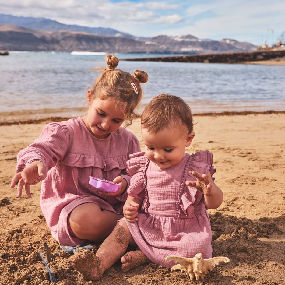 Dve devojčice u roze haljinama igraju se u pesku na plaži.