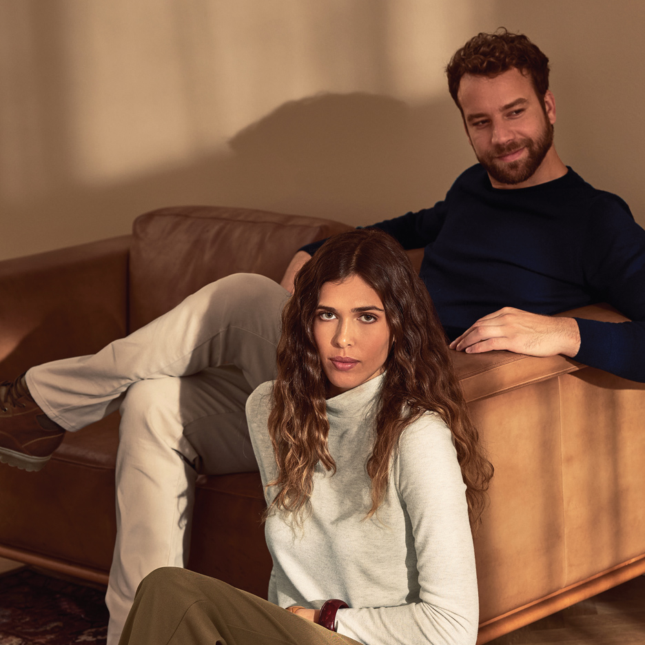 Muškarac u tamnoplavom džemperu i žena u svetlosivom džemperu sa rolkom sede na kauču.