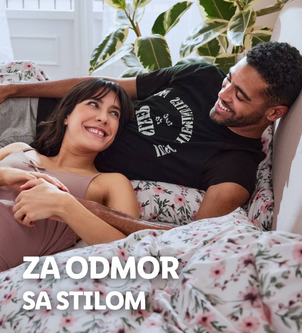 Par leži u krevetu sa cvetnim posteljinom, uživajući u odmoru sa stilom.