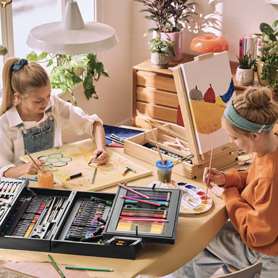 Dve devojčice slikaju i crtaju sa setovima za umetnost i štafelajem na stolu.