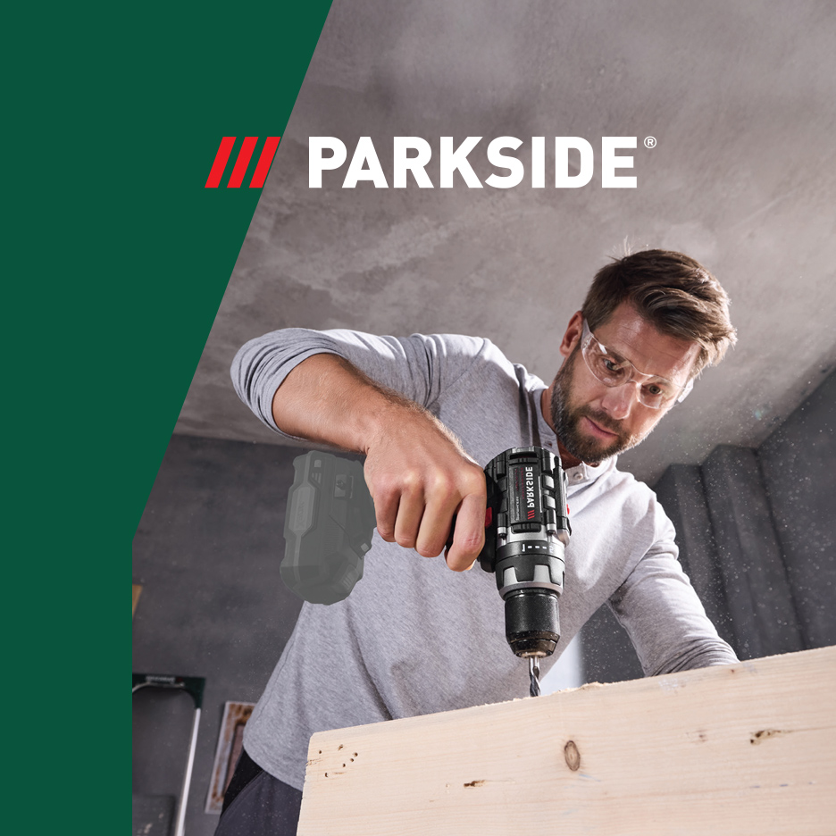 Muškarac u zaštitnim naočarima buši drvo Parkside bušilicom.