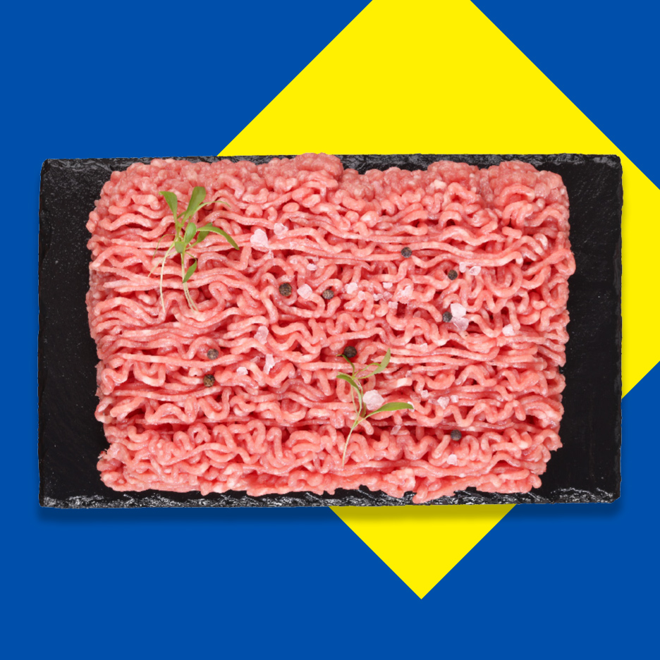 Sveže mleveno meso sa začinima na crnoj ploči, na plavo-žutoj pozadini.