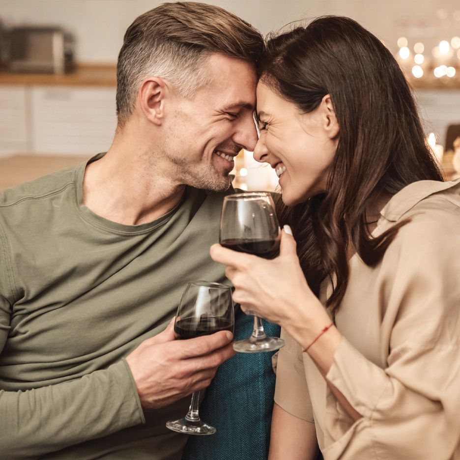Srećan par nazdravlja crvenim vinom, smejući se i dodirujući čela.