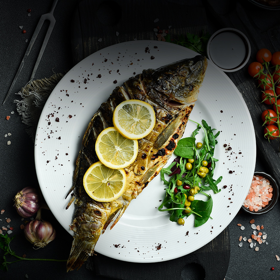 Grilovana riba sa limunom i salatom na belom tanjiru.