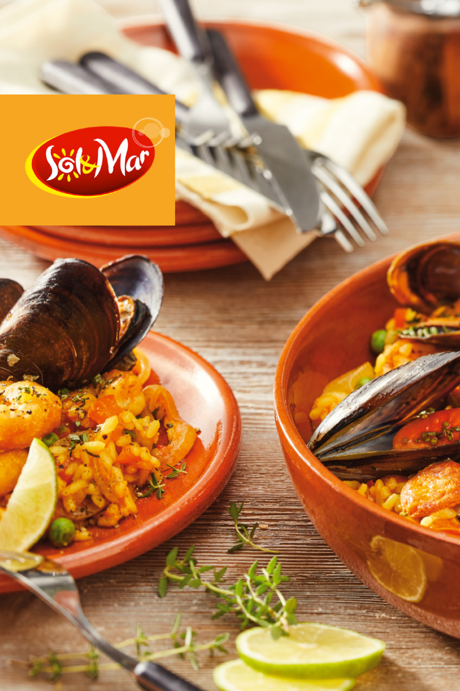 Dva tanjira paelje sa morskim plodovima, ukrašena limetom i timijanom, na drvenom stolu.