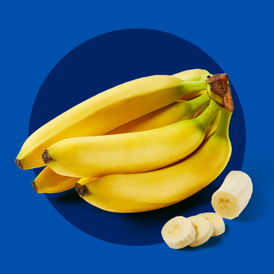 Zreli žuti grozd banana sa nekoliko isečenih kolutova na plavoj pozadini.