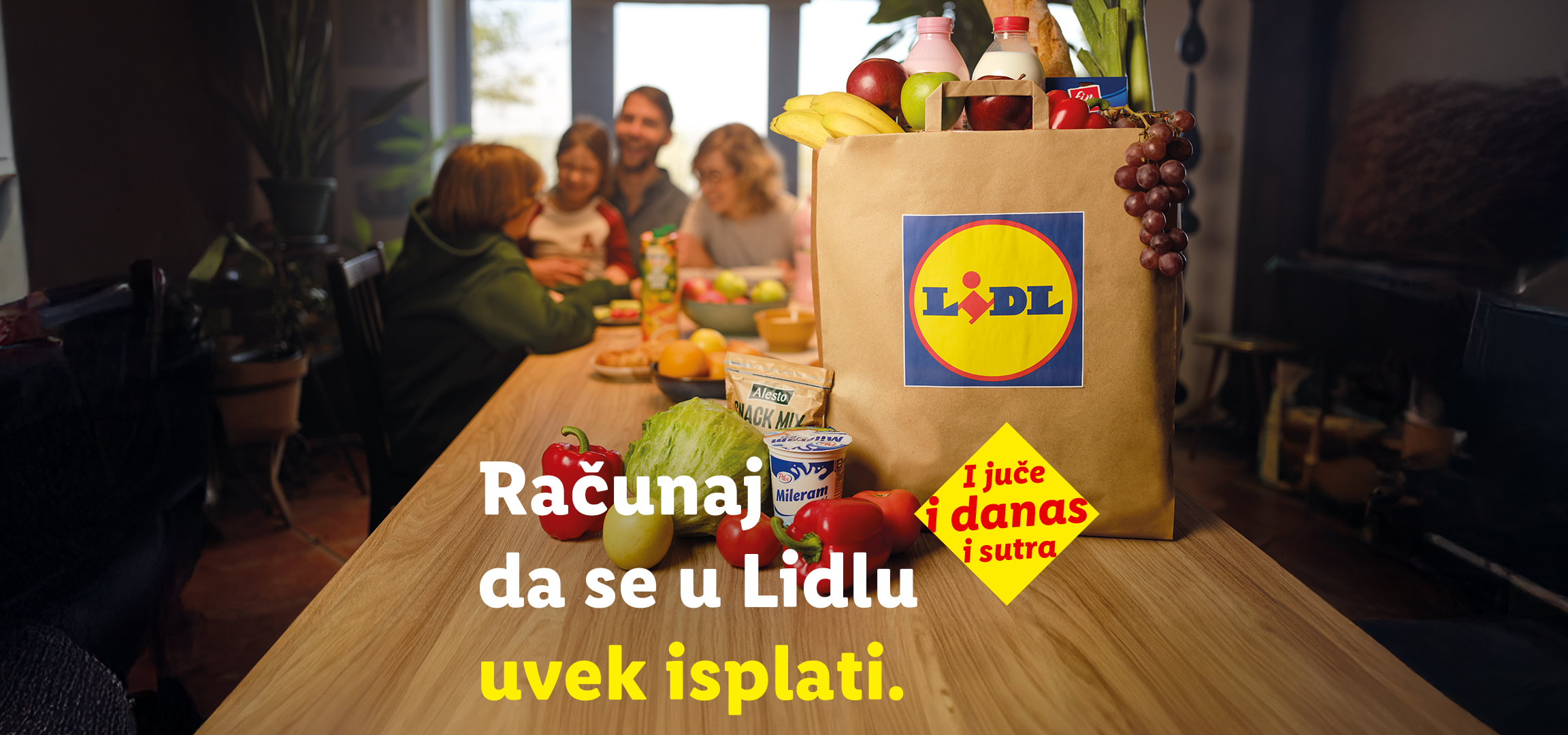 Porodica za stolom sa torbom punom namirnica iz Lidla, uključujući voće, povrće i mlečne proizvode, sa tekstom „Računaj da se u Lidlu uvek isplati. I juče i danas i sutra.“