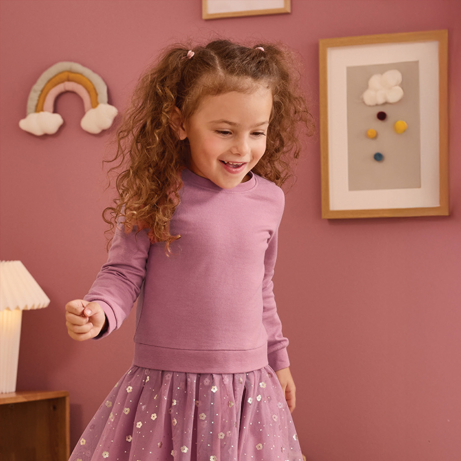 Devojčica u ljubičastoj majici i suknji sa šljokicama, smeje se u dečijoj sobi.