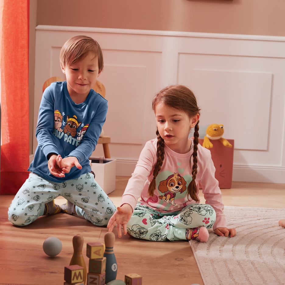 Dvoje dece u Paw Patrol pidžamama igraju se na podu.